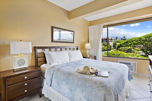 Habitación de hotel con cama, mesita de noche, ventana con vista a un paisaje exuberante y un cuadro en la pared.