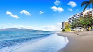 A beach with a clear view of the ocean, a sandy shore, and a modern building with balconies overlooking the beach. - Fall Special! Oceanview 1bd/2ba $195n (9/1 - 10/31) SK 231 - Sullivan (Lahaina)