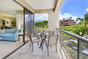 Un balcón con mesa y sillas, un sofá, y vistas a zonas verdes y edificios.