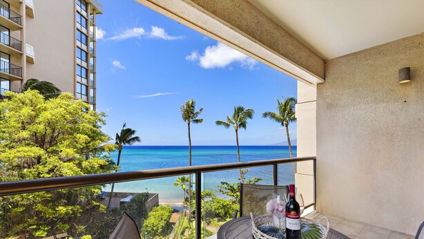 A balcony with a table, a bottle of wine, and a view of the ocean and palm trees. - Fall Special! Oceanview 1bd/2ba $195n (9/1 - 10/31) SK 231 - Sullivan (Lahaina)