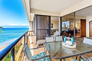 Uma varanda com mesa de vidro, cadeiras e vista para o oceano.