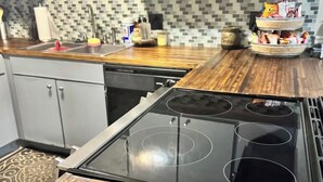 Keittiössä on puinen työtaso, musta liesi, jossa on neljä keittolevyä, ja laatoitettu seinä liesen takana.