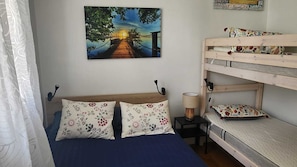 A bedroom with a bunk bed, a bed with floral pillows, a painting of a sunset over a bridge, and a small table with a lamp. - Oceanfront apartment, opposite family beach. (Capbreton)