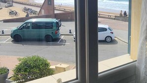 A view from a window overlooking a beach with parked vehicles and bicycles. - Oceanfront apartment, opposite family beach. (Capbreton)