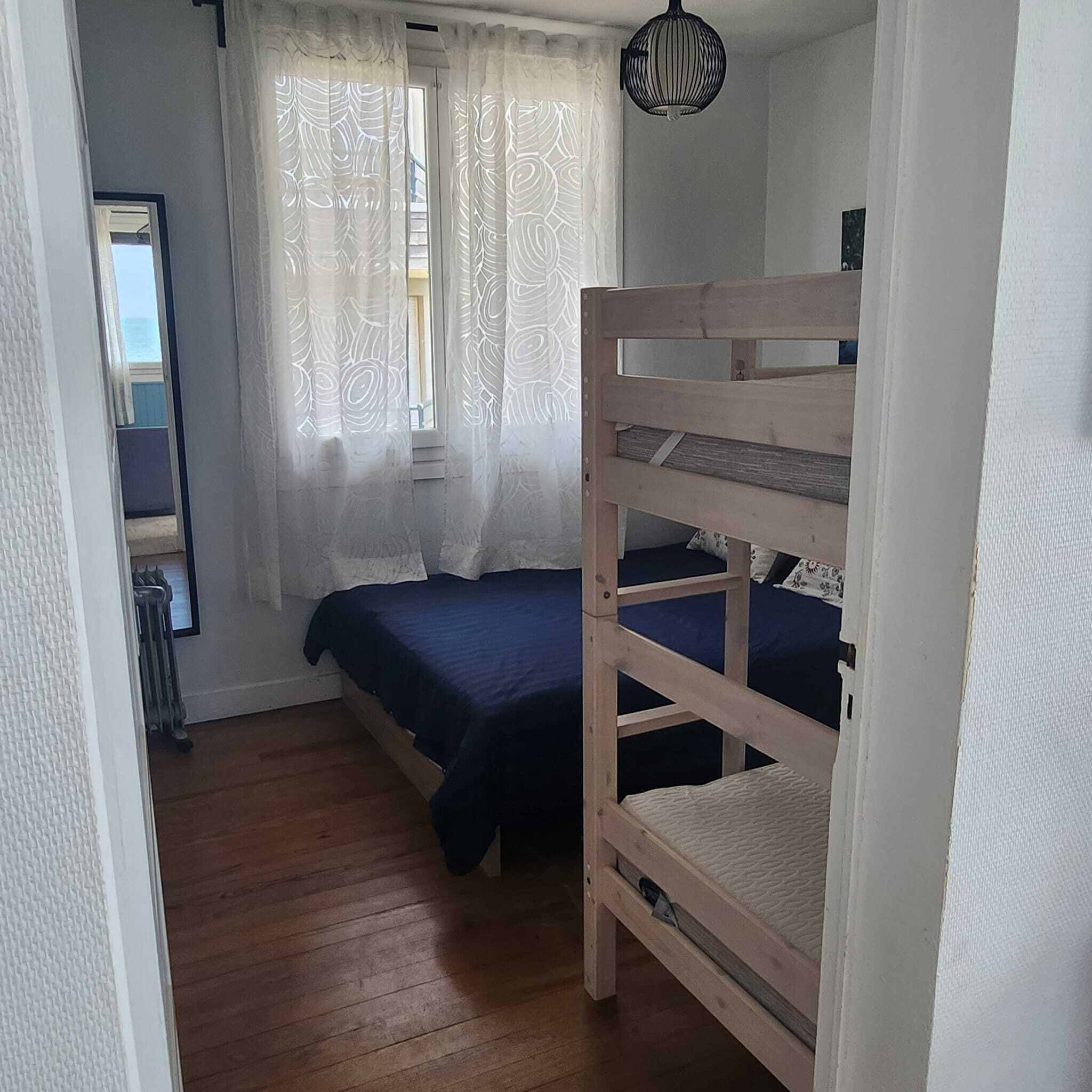 Une petite chambre individuelle avec un lit superposé, un radiateur et une fenêtre ornée de rideaux à motifs.