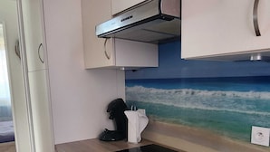 A modern kitchen with a black induction cooktop, white cabinets, and a beach mural on the wall. - Oceanfront apartment, opposite family beach. (Capbreton)