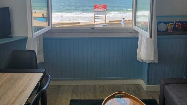 A room with a large window overlooking a beach, a wooden table, and a chair. - Oceanfront apartment, opposite family beach. (Capbreton)