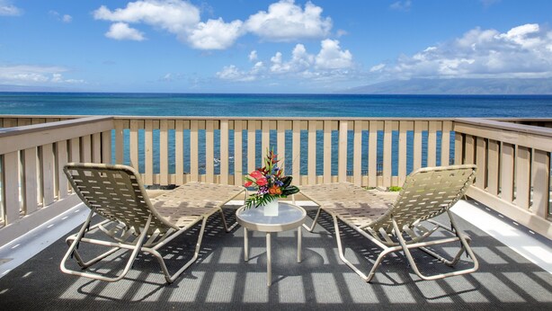 Een balkon met twee stoelen en een kleine tafel, met uitzicht op een heldere blauwe zee en een houten hek.
