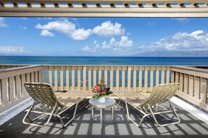 Ein Balkon mit zwei Stühlen und einem kleinen Tisch, mit Blick auf das klare, blaue Meer und einen Holzzaun.