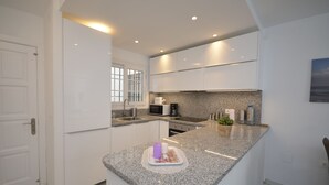A modern kitchen with white cabinetry, granite countertops, and a breakfast bar. - Apartment close to the beach in La Duquesa (Manilva)