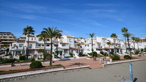 A coastal residential area with white buildings, palm trees, and a clear blue sky. - Apartment close to the beach in La Duquesa (Manilva)