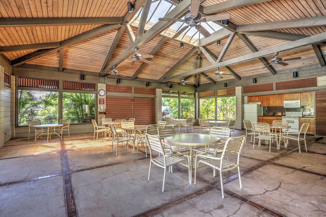 Un vaste patio couvert doté de plusieurs tables et chaises, de grandes fenêtres et d’un coin cuisine.