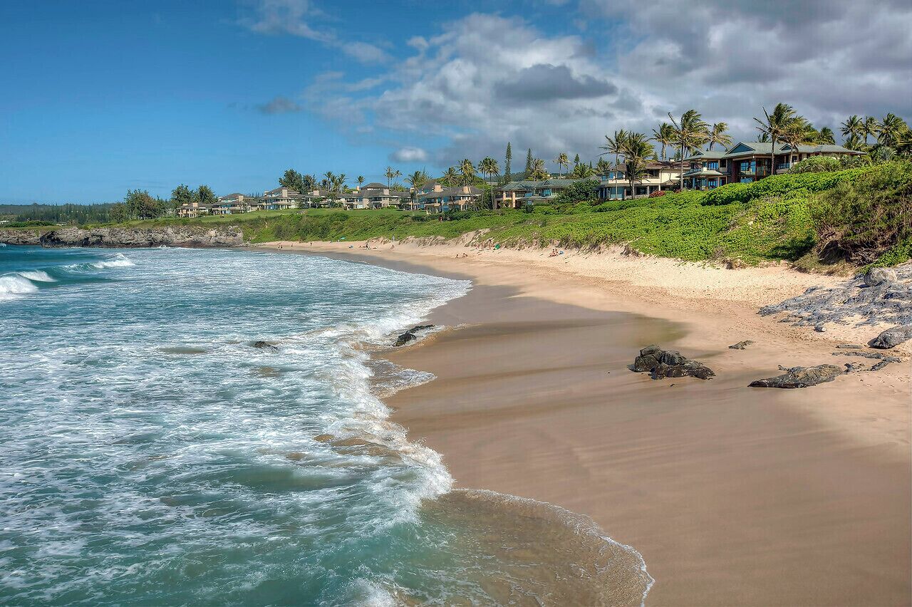 A beachfront property with ocean views, a sandy beach, and a hillside with houses.