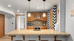 A kitchen with a granite island, wooden cabinets, and pendant lighting.