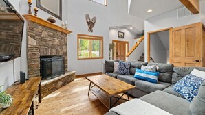 A spacious living room with a stone fireplace, a large gray sectional sofa, and a wooden coffee table.