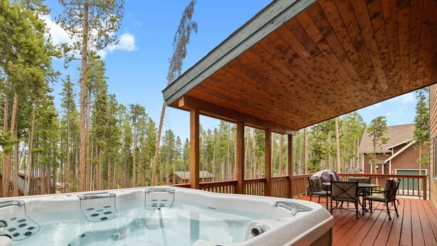 A hot tub on a wooden deck with a view of tall pine trees.