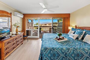 A bedroom with a bed, a TV, a desk, and a balcony with a view of the mountains.