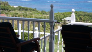 A balcony with white railings and two wooden chairs. The view includes a beach and the ocean. - Home-styled cottage on Nevis with spectacular views of the Caribbean Sea  (Nevis)