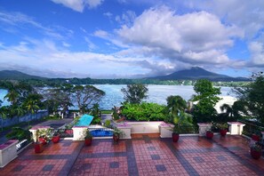 A rooftop terrace with potted plants, a swimming pool, and a view of a lake and mountains. - Ang Tahanan ni Aling Meding Hotel (San Pablo)