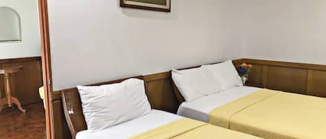 Habitación de hotel con dos camas individuales, cabecero de madera, un cuadro en la pared y una mesita con un florero.