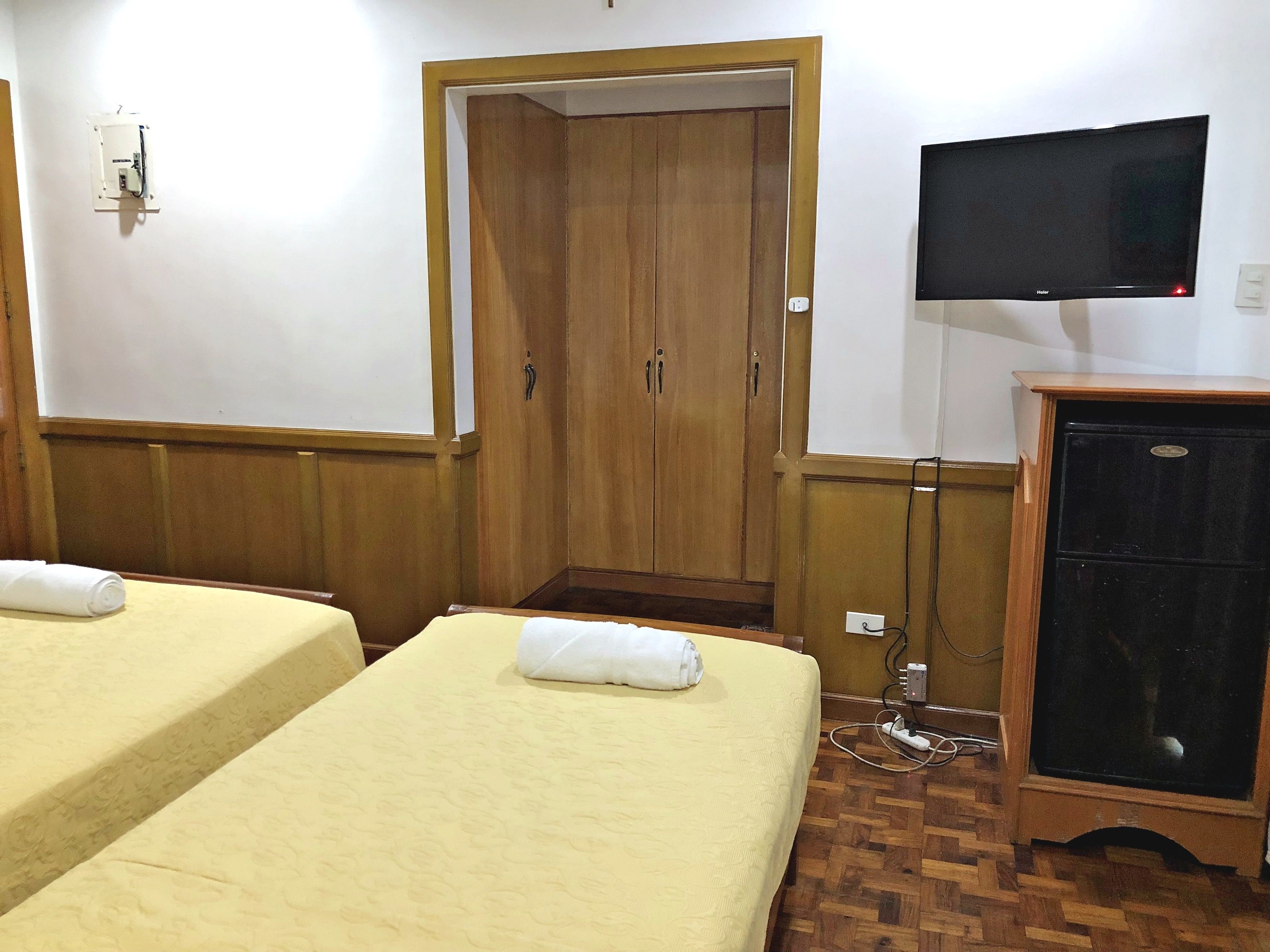 Una habitación de hotel con dos camas, un armario de madera, un televisor y un enchufe.
