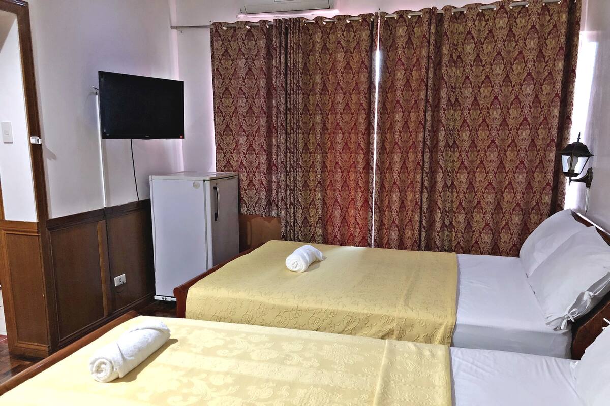 Une chambre d’hôtel avec deux lits, une télévision, un réfrigérateur et des rideaux à motifs.