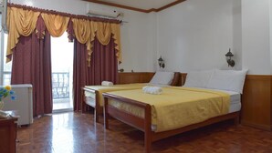 Habitación de hotel con dos camas, suelo de madera, ventilador de techo y balcón con cortinas.