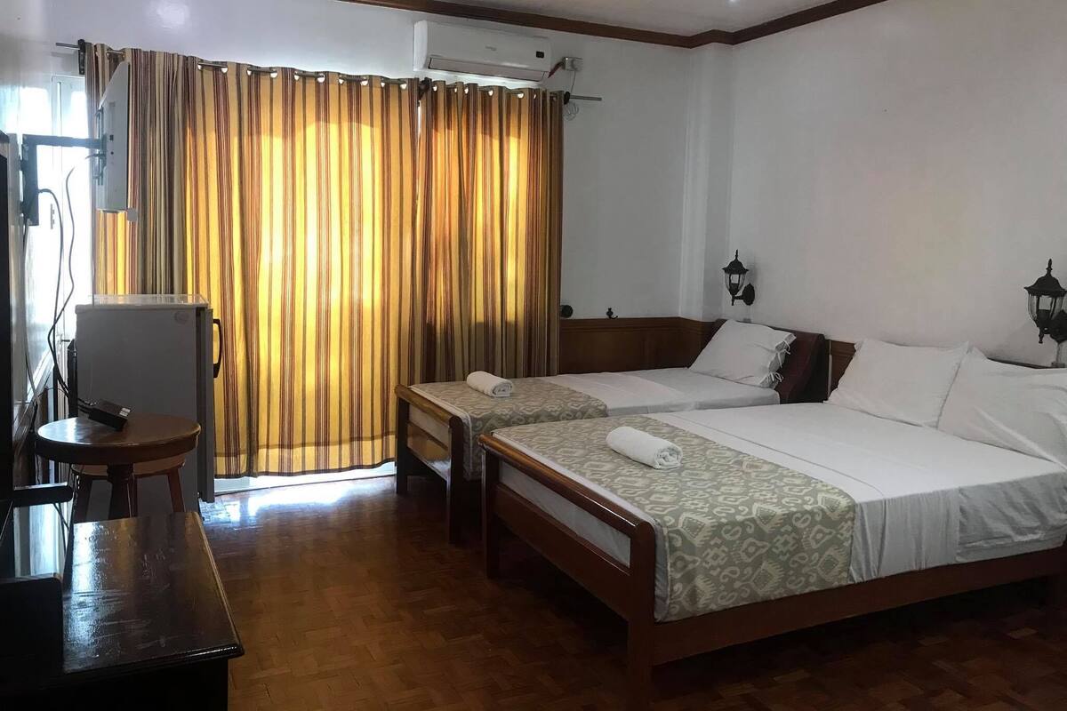 Une chambre d’hôtel avec deux lits, un bureau, un ventilateur de plafond et une fenêtre avec des rideaux.