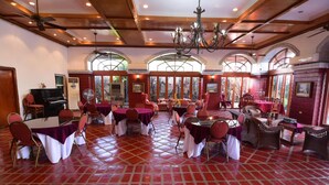 Un comedor amplio con varias mesas y sillas, ventanas grandes con arcos y un piso de baldosas rojas.