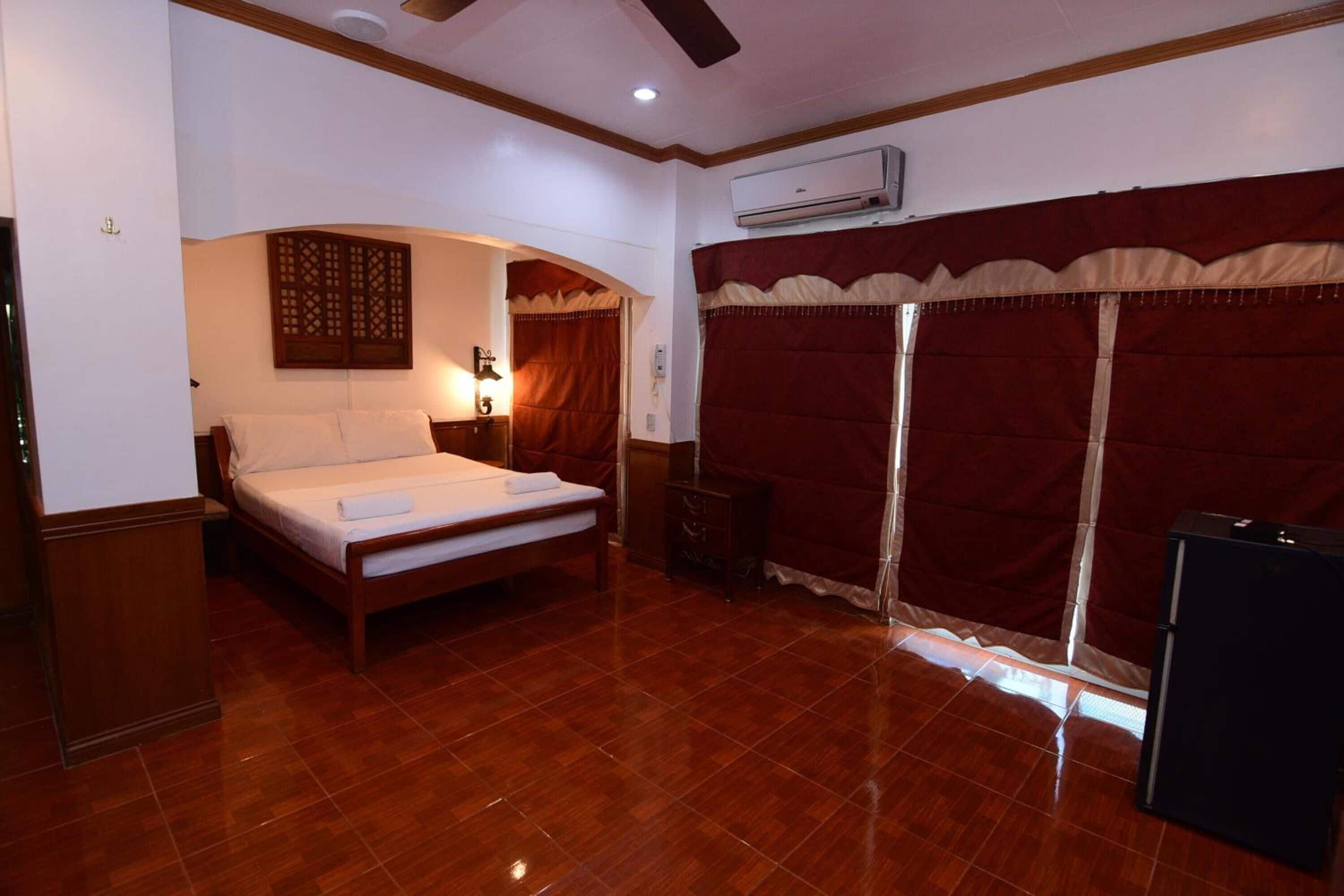 Un dormitorio con una cama de madera, una mesita de noche, aire acondicionado instalado en la pared y una cortina roja.