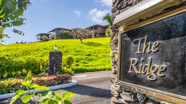 A sign reading "The Ridge" with a stone wall and greenery in the background.