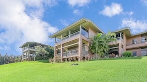 A multi-story residential building with balconies, a well-maintained lawn, and surrounding greenery.
