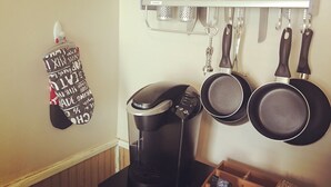 Et køkken med kaffemaskine, hængende gryder og et krydderihylder.