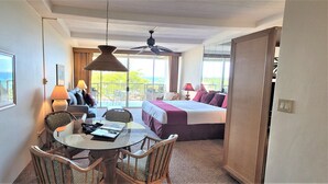 Habitación de hotel con balcón, cama, mesa de comedor y sillas, y ventilador de techo.