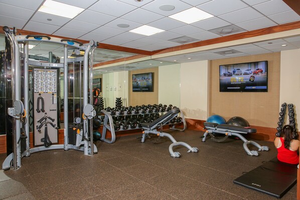 A gym with exercise equipment, a mirror, and a television on the wall.
