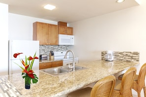 A modern kitchen with granite countertops, stainless steel appliances, wooden cabinets, and a built-in microwave.