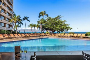 A poolside area with lounge chairs and a table with glasses, overlooking a clear blue pool and ocean view.