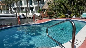 Una piscina con barandilla de metal, rodeada de palmeras y un edificio con balcones.
