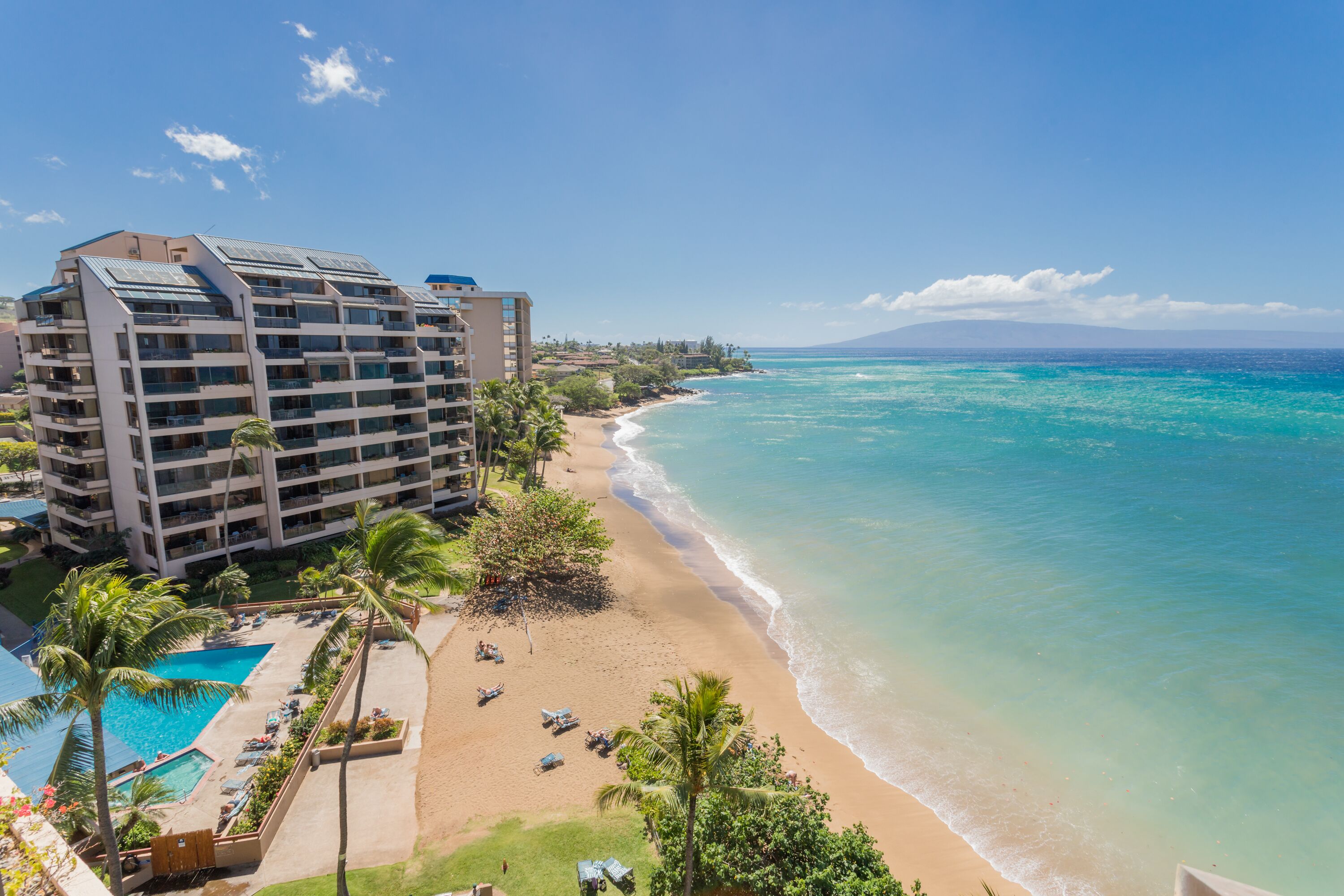 Un hôtel situé en bord de mer, doté d’une piscine, de chaises longues et de palmiers.
