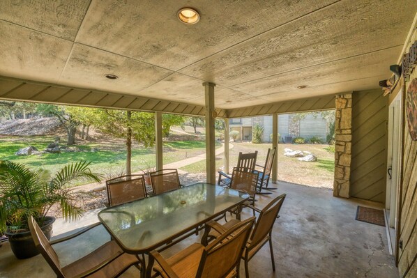 A covered patio with a glass table and chairs, a stone pillar, and a view of a landscaped yard.