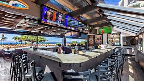 Zona de bar con una barra alargada, diversas opciones de asiento y vista a la playa.
