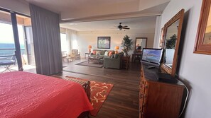 Ein Hotelzimmer mit einem großen Bett, einem Fernseher, einer Sitzecke mit Couchtisch und einem Balkon mit Meerblick.