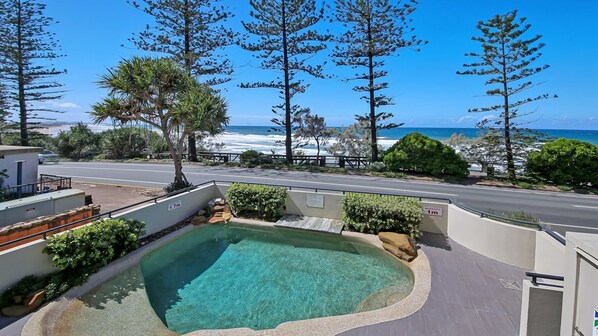 A swimming pool with a view of the ocean, surrounded by trees and a road. - Unit 2 'The Rocks', Coolum Beach (Coolum Beach)