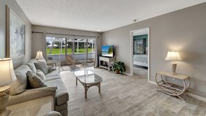 Un salon spacieux avec un canapé, une table basse et un téléviseur, de grandes fenêtres et un balcon.