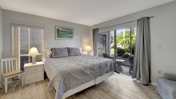 Une chambre à coucher comprenant un lit, des tables de chevet, un banc et une vue sur l’extérieur grâce à de grandes fenêtres.