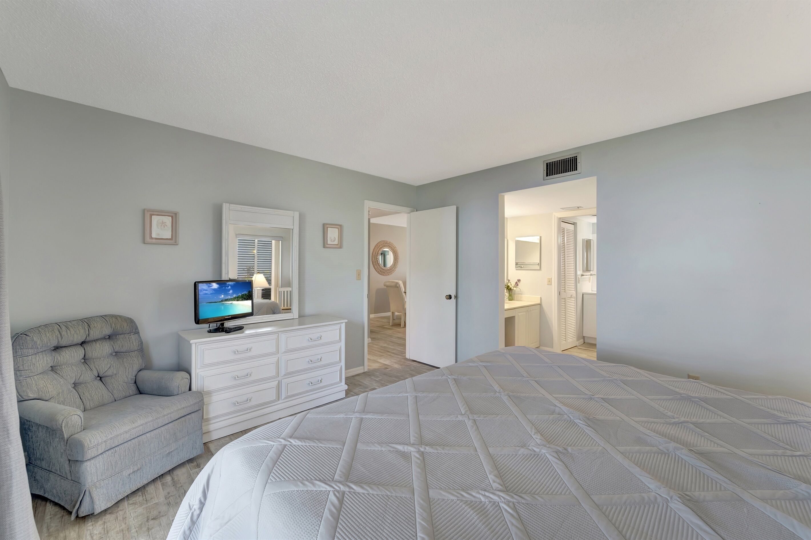 Un dormitorio con cama, televisor en una cómoda, una silla y una puerta que da a un baño.