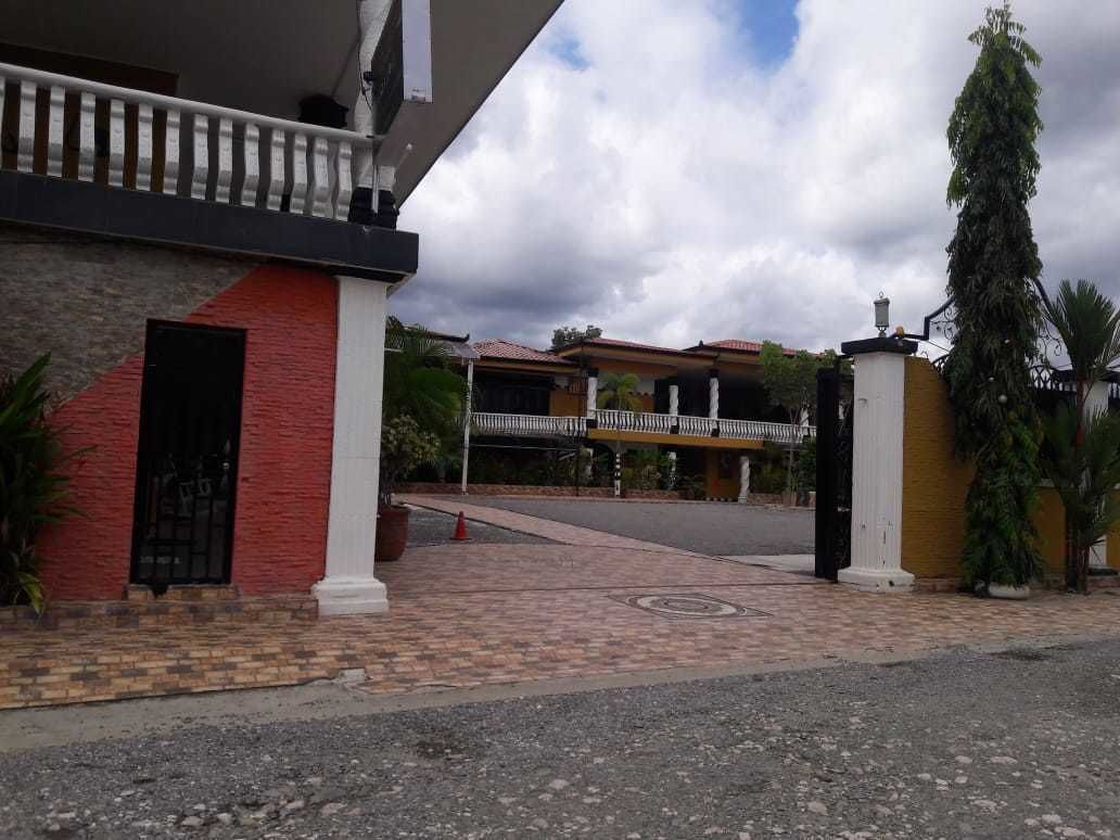 A building entrance with a gated driveway, a covered walkway, and a tall tree.