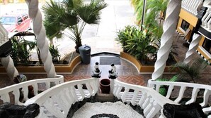 Una escalera con barandillas blancas, un diseño circular de piedra en la parte inferior y vegetación circundante.