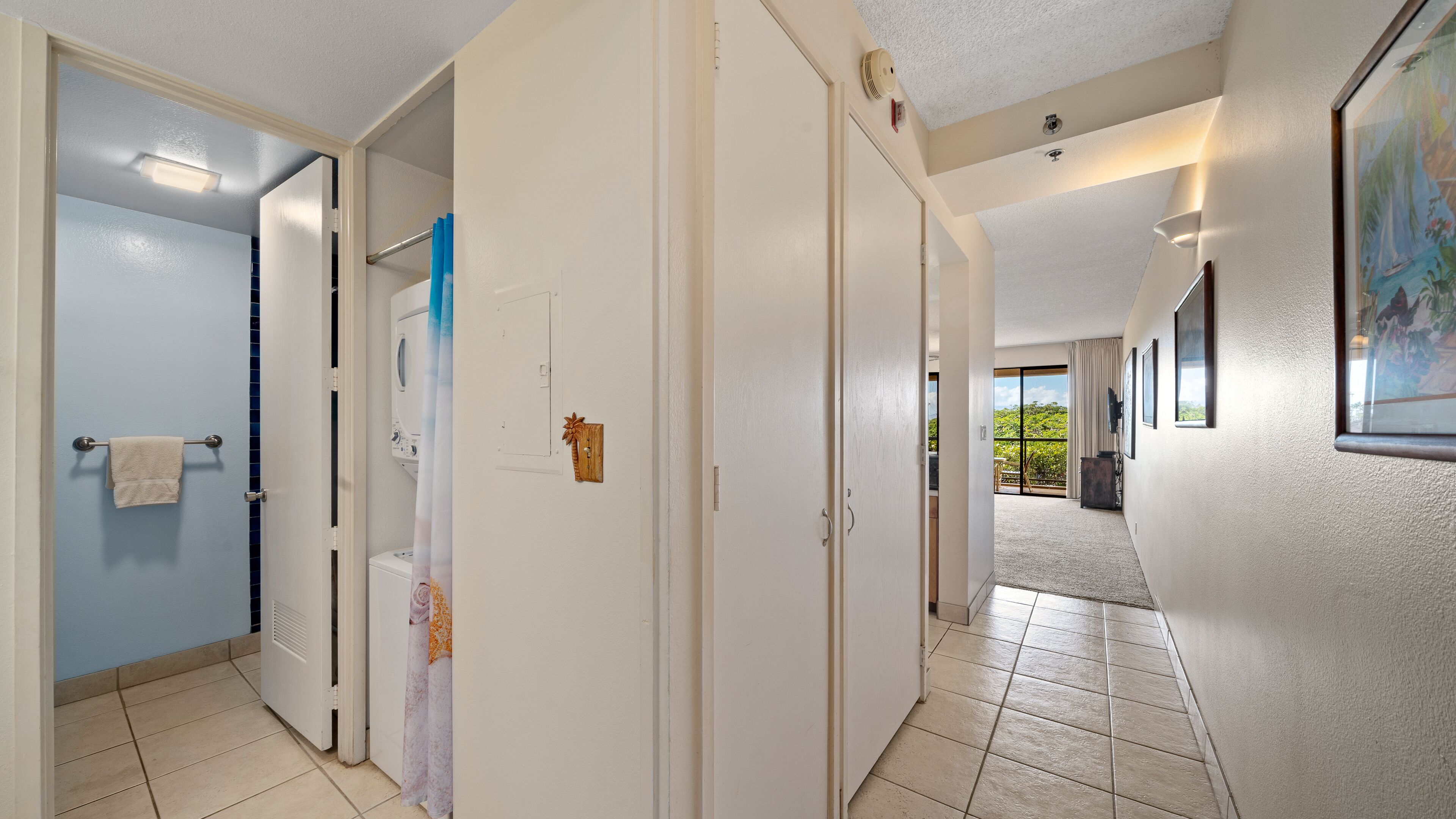 A hotel hallway with a view to a balcony, a door with a towel rack, and a wall-mounted light fixture.