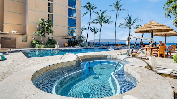 A hotel pool area with a hot tub, lounge chairs, and a view of the ocean.